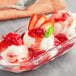 A bowl of Oringer strawberry sundae topping on ice cream with strawberries and a mint leaf.