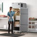 A woman wearing an apron opening a Delfield reach-in freezer in a school kitchen.