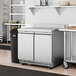 An Avantco stainless steel worktop refrigerator with a backsplash on a counter in a commercial kitchen.