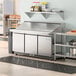 An Avantco stainless steel 3 door refrigerated sandwich prep table on a large counter in a commercial kitchen.