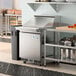 An Avantco refrigerated sandwich prep table on a stainless steel counter in a commercial kitchen.