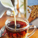 A glass cup of coffee with Pacific Foods Ultra Soy Milk being poured into it.