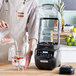 A man pouring milk into a Hamilton Beach Summit Edge blender on a counter.