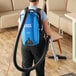 A person in a blue shirt using a Lavex backpack vacuum cleaner to vacuum a room.