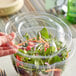 A person's hand using a clear Stalk Market lid on a plastic salad container.