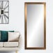 A BrandtWorks champagne finish mirror on a white wall above a white couch with green pillows.