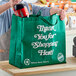 A woman putting a bottle of soda into a green RediBag USA reusable shopping bag.