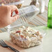 A hand holding a Stalk Market clear plastic hinged container of salad.