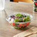 A clear plastic bowl filled with salad and a lid with a wooden fork on a table.