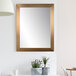 A BrandtWorks champagne finish mirror on a white wall above a chair.