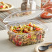 A person using a black spoon to take pasta from a Stalk Market clear plastic deli container.