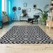 A Couristan Afuera Dipole area rug with black and white geometric patterns on a floor with a chair and a shelf.