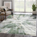 A green and gray contemporary splash area rug with a modern design in a room with a wooden chair and a plant.