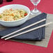 A bowl of noodles with Town ivory plastic chopsticks next to a glass of water.