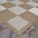 A Couristan light brown and ivory checkered area rug on a stone floor.