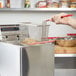 A hand using a metal basket with red handles to fry potatoes in a Cecilware countertop deep fryer.