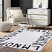 A cream rug with black alphabet letters on it in a white room.