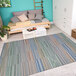 A Couristan Cape Shoreham ivory multi-color area rug with blue and white stripes in a room with a bed.