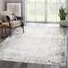 A white and green Abani Atlas Collection area rug in a room with a wooden chair and a plant.