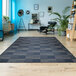 A Couristan Afuera Regatta marine and shell area rug with a blue and black pattern in a room with a chair and plant.