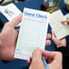 A person using a blue pen to fill out a Choice Green and White Guest Check on a counter.