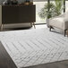 A cream and grey Abani Casa Collection Moroccan trellis area rug in a room with a white couch and potted plants.
