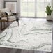 A green and gray Abani Atlas Collection area rug with a contemporary abstract marble design in a room with a wooden floor and a plant.