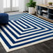 A navy and cream rectangular area rug with a geometric design in a room with a blue cushion on a white surface.