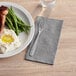 A plate of food with a fork and a black linen-feel dinner napkin on a table.