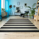 A Couristan Afuera Yacht Club onyx and ivory striped area rug on a wood floor with a chair and a plant.