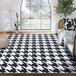 An Abani Parker Collection black and white houndstooth area rug in a white room with a couch and a tree.