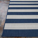 A Couristan Afuera Yacht Club area rug with blue and white stripes on a stone surface.