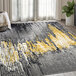 A metallic drip patterned Abani Arto Collection area rug in gray, yellow, black, and white on a white floor.