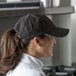 A woman in a Chef Revival black embroidered 6-panel baseball cap standing in a professional kitchen.