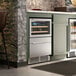 A dual temperature beverage cooler with a glass door top section for bottles and a stainless steel bottom drawer, built into a kitchen counter.