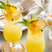 A couple of glasses of drinks with a yellow liquid and pineapple garnish.