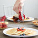 A person using a Tablecraft glass syrup dispenser to pour syrup on a stack of pancakes.