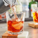 A close-up of a drink being poured into an Anchor Hocking Clarisse Rocks glass filled with ice.