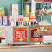 A man using a metal ladle to pour sauce onto a hot dog from a Carnival King double condiment warmer.