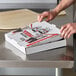 A man opening a Choice white corrugated pizza box on a counter.