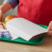 A person holding a white box with a Carnival King White Kraft Paper Food Sleeve on a tray with a sandwich and a drink.