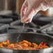 A gloved hand sprinkling Regal Organic Granulated Onion onto a pan of food.