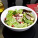 A white bowl filled with salad and fruit.