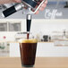 A hand using a Whip-It stainless steel nitro brew whipper to pour brown liquid into a glass.