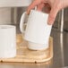 A person using a Cambro beige cup stacker to carry white mugs.