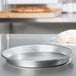 An American Metalcraft aluminum pizza pan on a counter with dough.