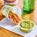 A small container of Sabra guacamole with rolled tortilla chips on a table.