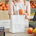 A person holding an orange in a white bag.