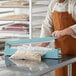 A man in an apron using an Omcan manual bag sealer.