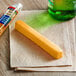 A Sargento Mild Cheddar cheese stick on a napkin next to a green bottle of beer.